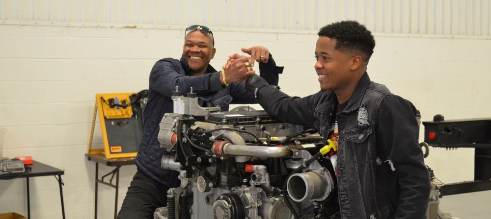Two african-american men work on a car motor at American Diesel Training Centers.